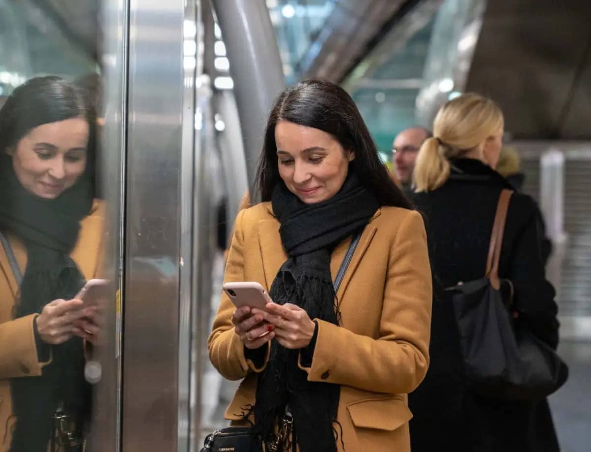 Photo d'une femme souriante qui regarde son téléphone dans le métro